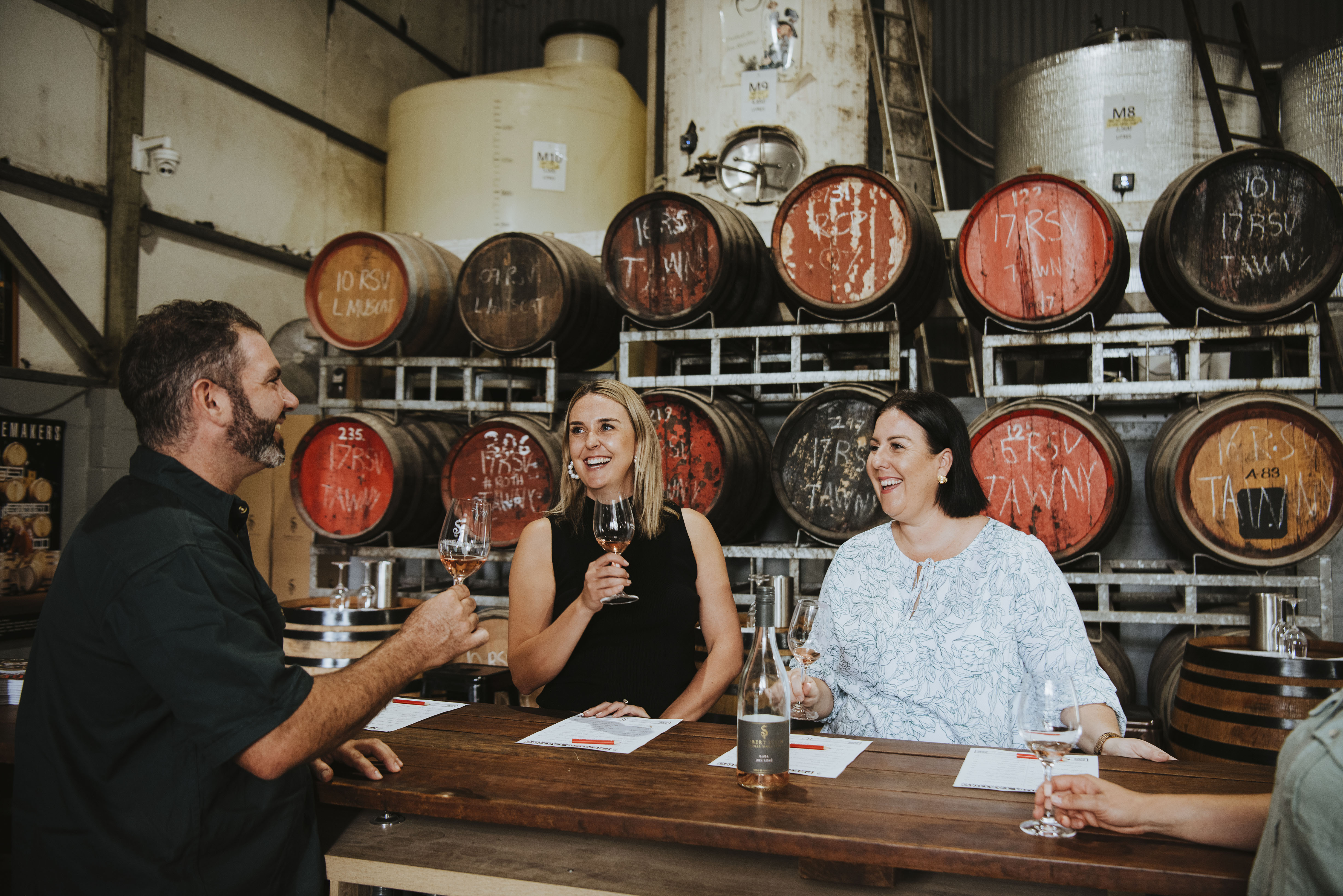 Four people doing a wine tasting in surrounded by barrels 